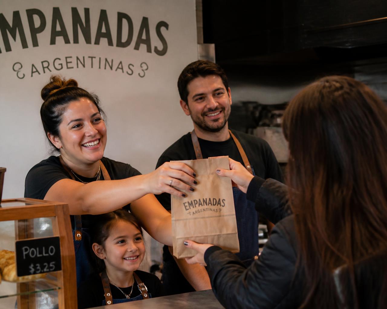 Staff handing a bag of empanadas across the counter to a customer